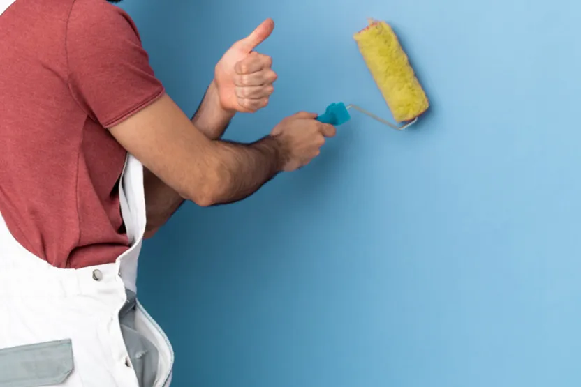 A man with a paint roller in hand, showing a thumbs up gesture.