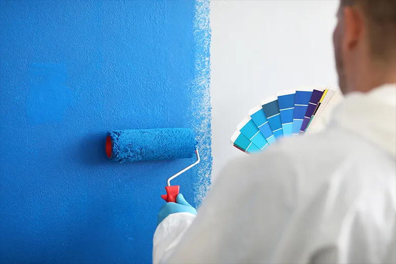 A man in white gloves carefully painting a blue wall with a brush, displaying precision and attention to detail.