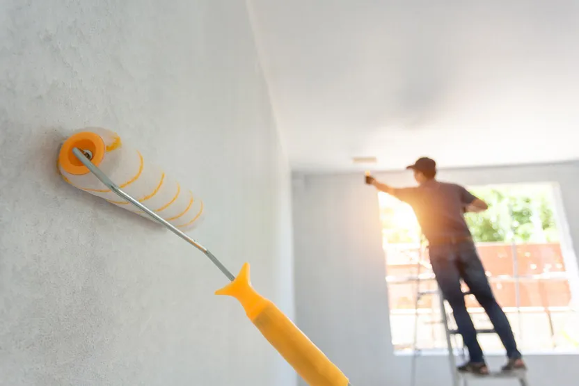 A man using a roller to paint a wall, adding color and texture to the surface with smooth strokes.